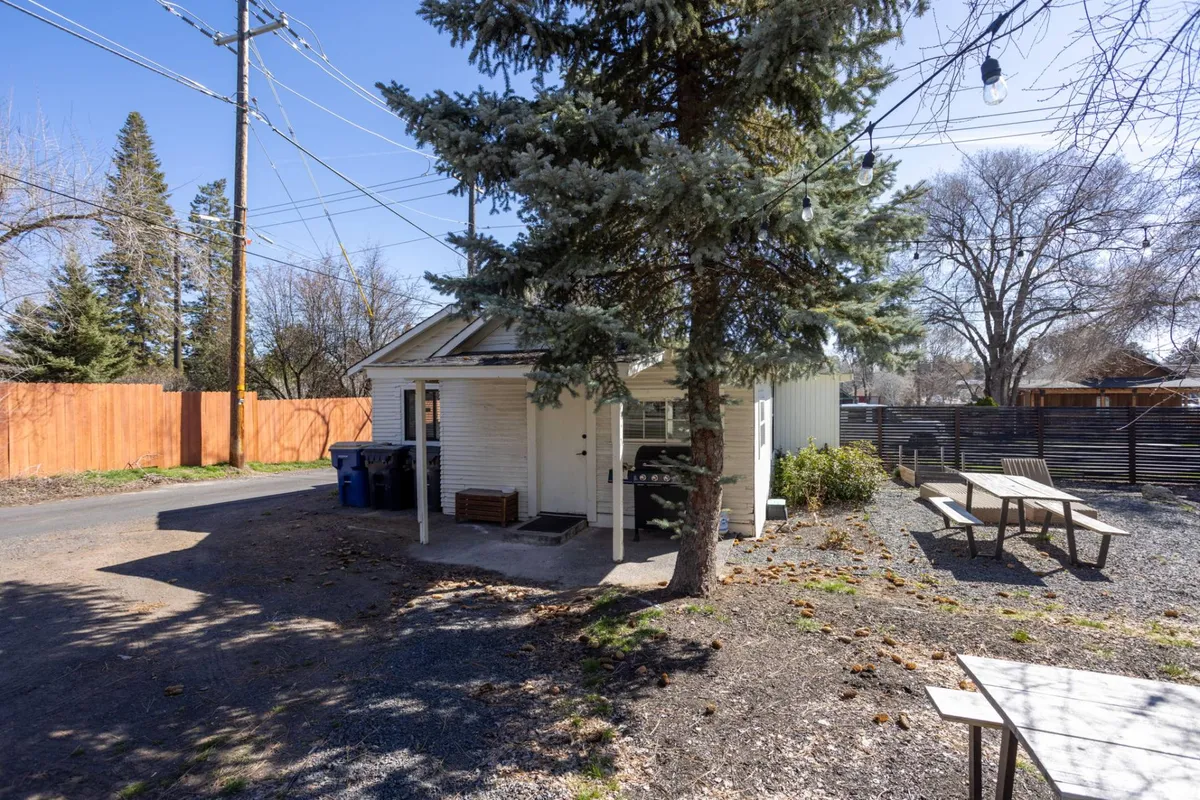 The exterior of the home with a large shade tree, picnic tables, and an inviting yard space. The setup is perfect for outdoor dining, relaxing under the tree, or casual gatherings, making it a welcoming environment for families and pets alike.