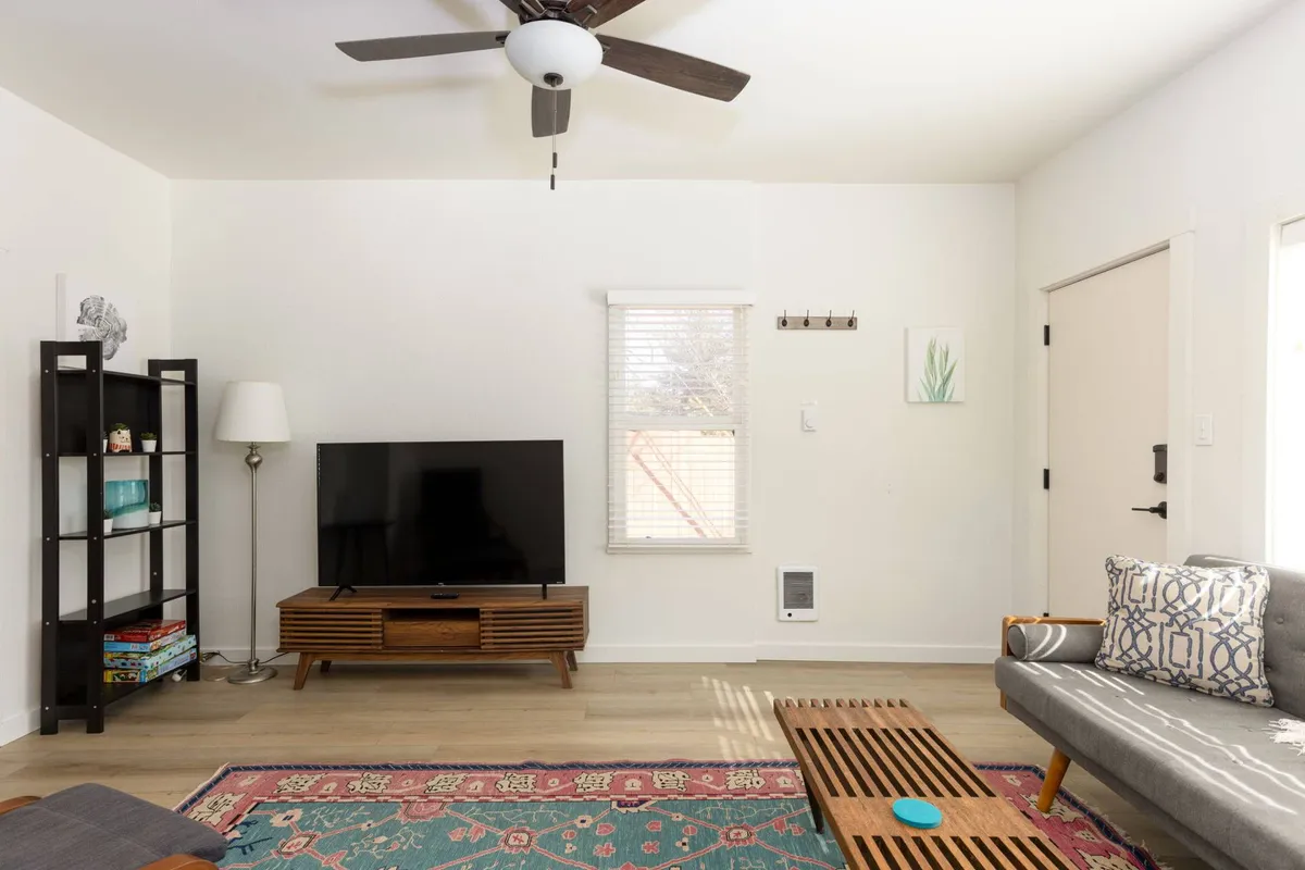 A sunlit living room featuring a comfortable sofa, a television, a coffee table, and a bookshelf. The seating is arranged to encourage conversation and relaxation, with ample natural light streaming in, making it perfect for socializing, movie nights, or reading.