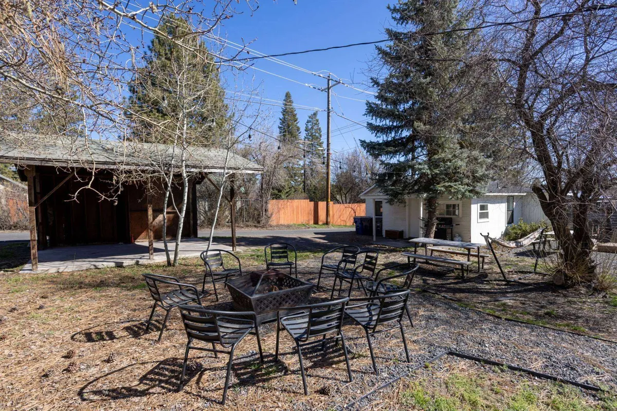 A welcoming outdoor space featuring a central fire pit with seating, an adjacent structure for shade, and trees providing a secluded, nature-filled backdrop. The scene is vibrant and ready for lively gatherings, barbecues, or quiet evenings by the fire.