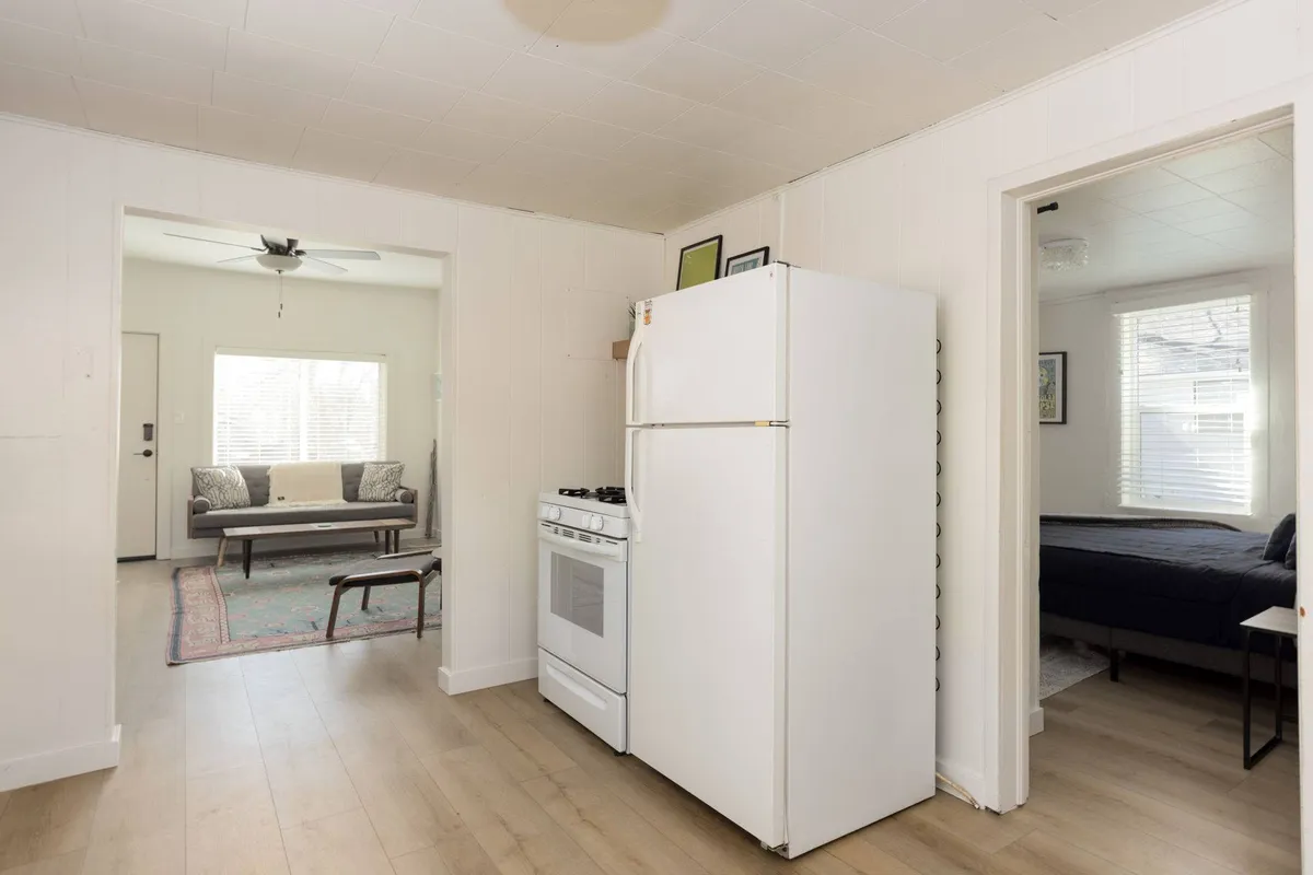 An inviting interior scene featuring a kitchen with appliances, a cozy living area, and a doorway leading towards a bedroom. The arrangement is homey and supports shared meals, entertaining guests, and relaxing evenings together—a natural setting for families or groups to connect.