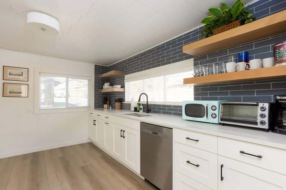A cozy kitchen scene highlighting the sink area, open shelving with neatly arranged dishes, and visible appliances. The room feels intimate, welcoming, and practical—encouraging relaxed meals and easy cleanup, as referenced in the content.