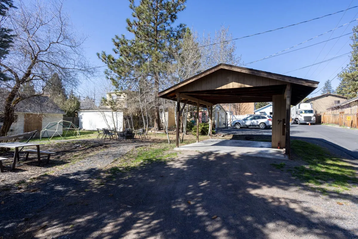 This image features the exterior of the property, showcasing a carport surrounded by trees and a gravel driveway. The setting suggests a welcoming entry point and ample space for parking, perfect for groups arriving together. The relaxed outdoor atmosphere hints at opportunities for outdoor gatherings and enjoying sunny afternoons.