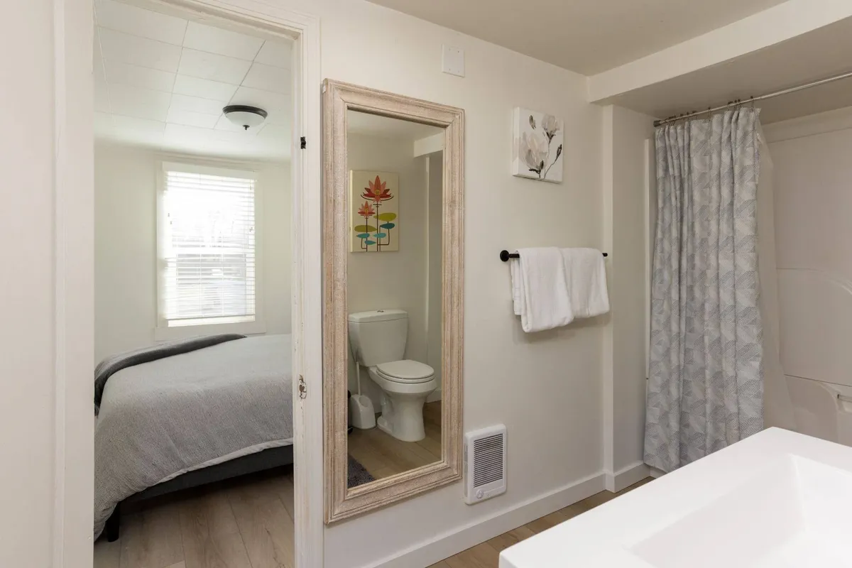 A bright bathroom showcasing a large mirror, toilet, and a shower with a curtain. The space feels calm, clean, and functional—ideal for personal grooming and relaxation. Ample lighting and uncluttered surfaces add to the comfort.