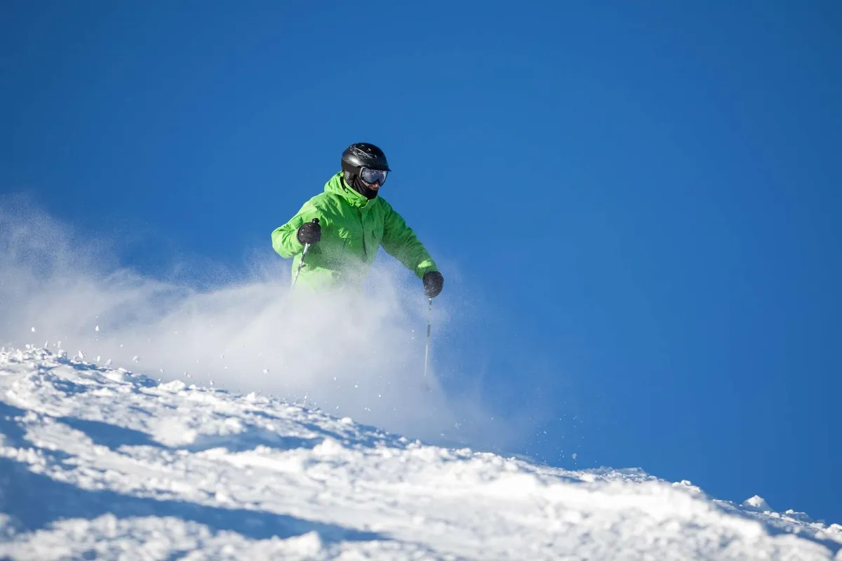 A skier descends a pristine, snow-covered slope under a clear blue sky. The image is filled with energy and captures both the thrill of winter sports and the majestic mountain backdrop, evoking the sense of freedom and exhilaration Bend offers in the colder months.